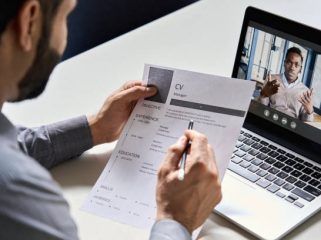 Male indian hr, recruiter or employer holding cv having online virtual job interview meeting with african candidate on video call. Distance remote recruitment conference chat. Over shoulder view.