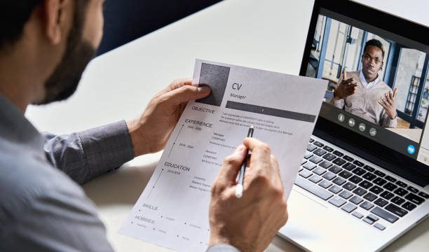 Male indian hr, recruiter or employer holding cv having online virtual job interview meeting with african candidate on video call. Distance remote recruitment conference chat. Over shoulder view.